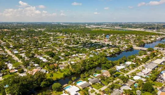 A residential area of Wilton Manors, Florida, with numerous houses, lush green trees, and canals winding through the neighborhood under a partly cloudy sky representing area of Plumber Wilton Manors.