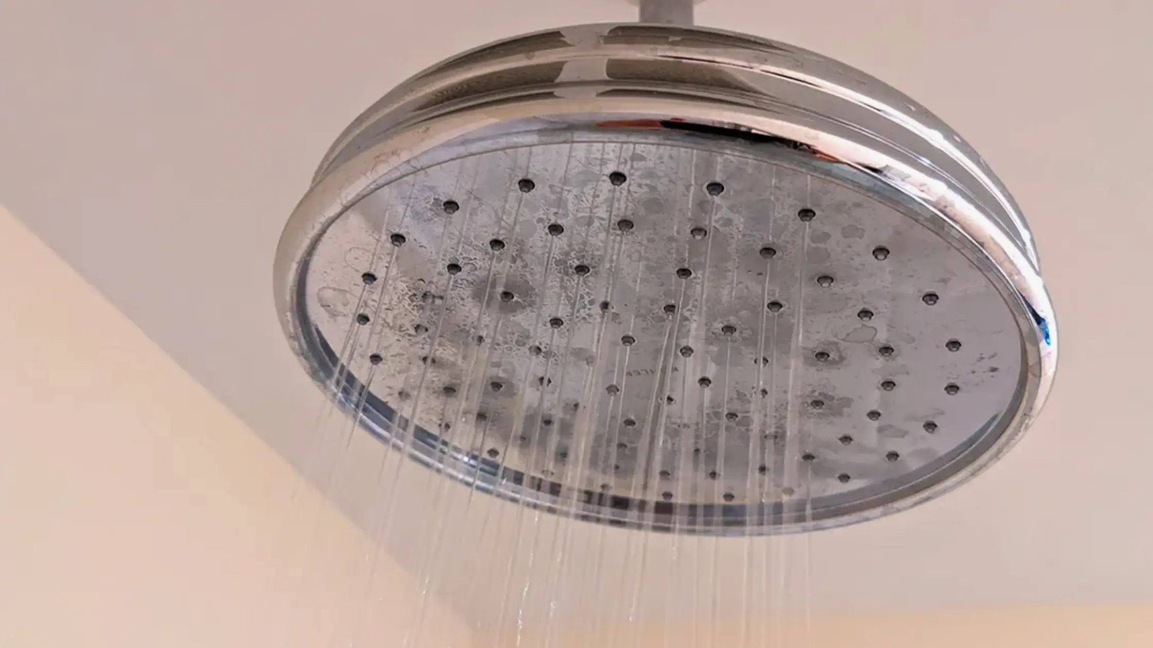  A shower head with visible mineral deposits sprays several weak streams of water, illustrating low water pressure.