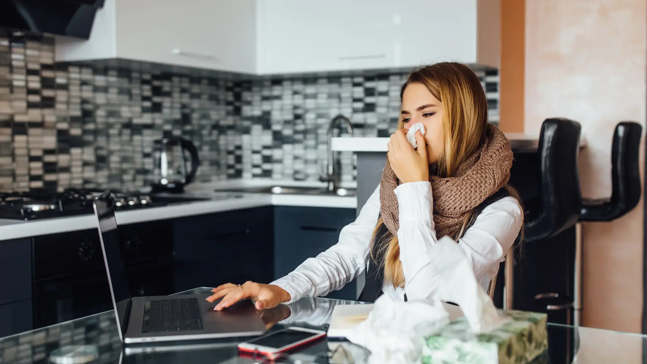 Woman sitting in kitchen holding tissue to her nose, illustrating how to distinguish gas odor from other smells.