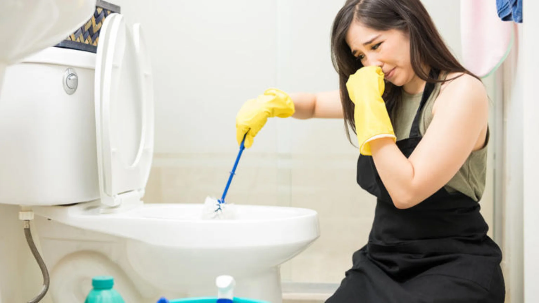 Woman cleaning toilet while holding nose, illustrating why bathroom smells like rotten eggs.